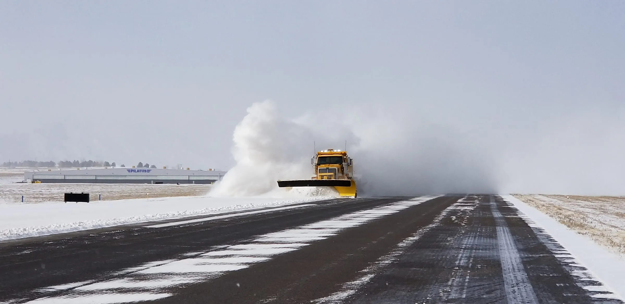 A yellow snowplow throwing a cloud of white snow across a runway at Rocky Mountain Metropolitan Airport in Broomfield on January 24, 2019